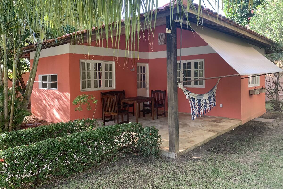 Una casa con fachada roja, un porche con mesa y sillas, y una hamaca.