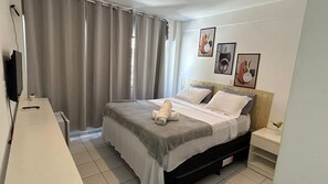 A bedroom with a bed, bedside tables, a desk, and curtains.