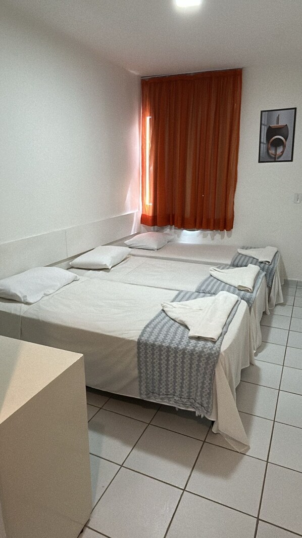 A room with two beds, a bedside table, a window with curtains, and a framed picture on the wall.