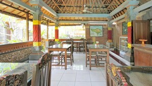 A restaurant with wooden tables and chairs, a tiled floor, and a ceiling with exposed beams. - Dewa Bharata Bungalow Ubud (Ubud)