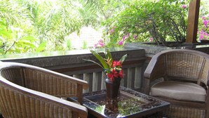 A patio area with wicker chairs and a glass-top table, surrounded by lush greenery and a decorative vase with flowers. - Dewa Bharata Bungalow Ubud (Ubud)