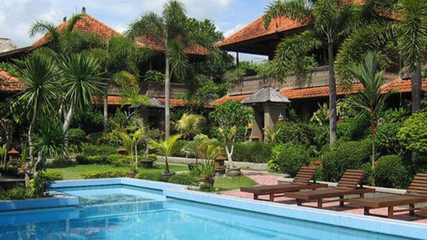 A swimming pool with lounge chairs, surrounded by lush greenery and traditional-style buildings with red-tiled roofs. - Dewa Bharata Bungalow Ubud (Ubud)
