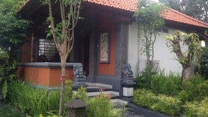 A traditional house with a tiled roof, a porch with steps, and a statue in front. - Dewa Bharata Bungalow Ubud (Ubud)