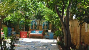 Un patio con un suelo de mosaico colorido, un banco de madera y diversas plantas en macetas.