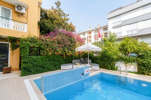 A swimming pool with a tiled edge, surrounded by greenery and a white umbrella. - Benna Hotel (Konyaalti)