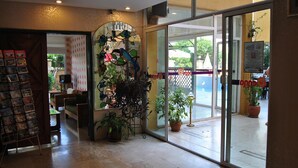 Un vestíbulo de hotel con una puerta de cristal, un mostrador de recepción y un reloj en la pared.