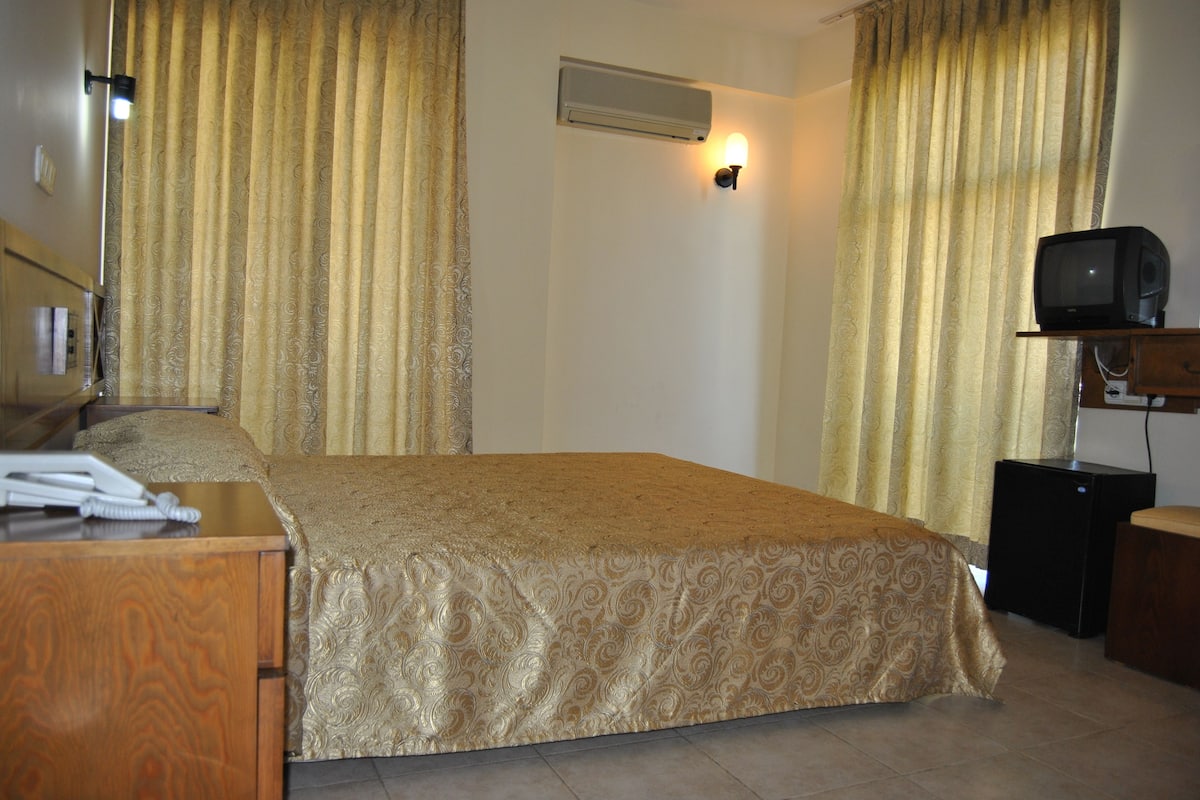 A hotel room with a bed, a desk, a television, and an air conditioning unit.