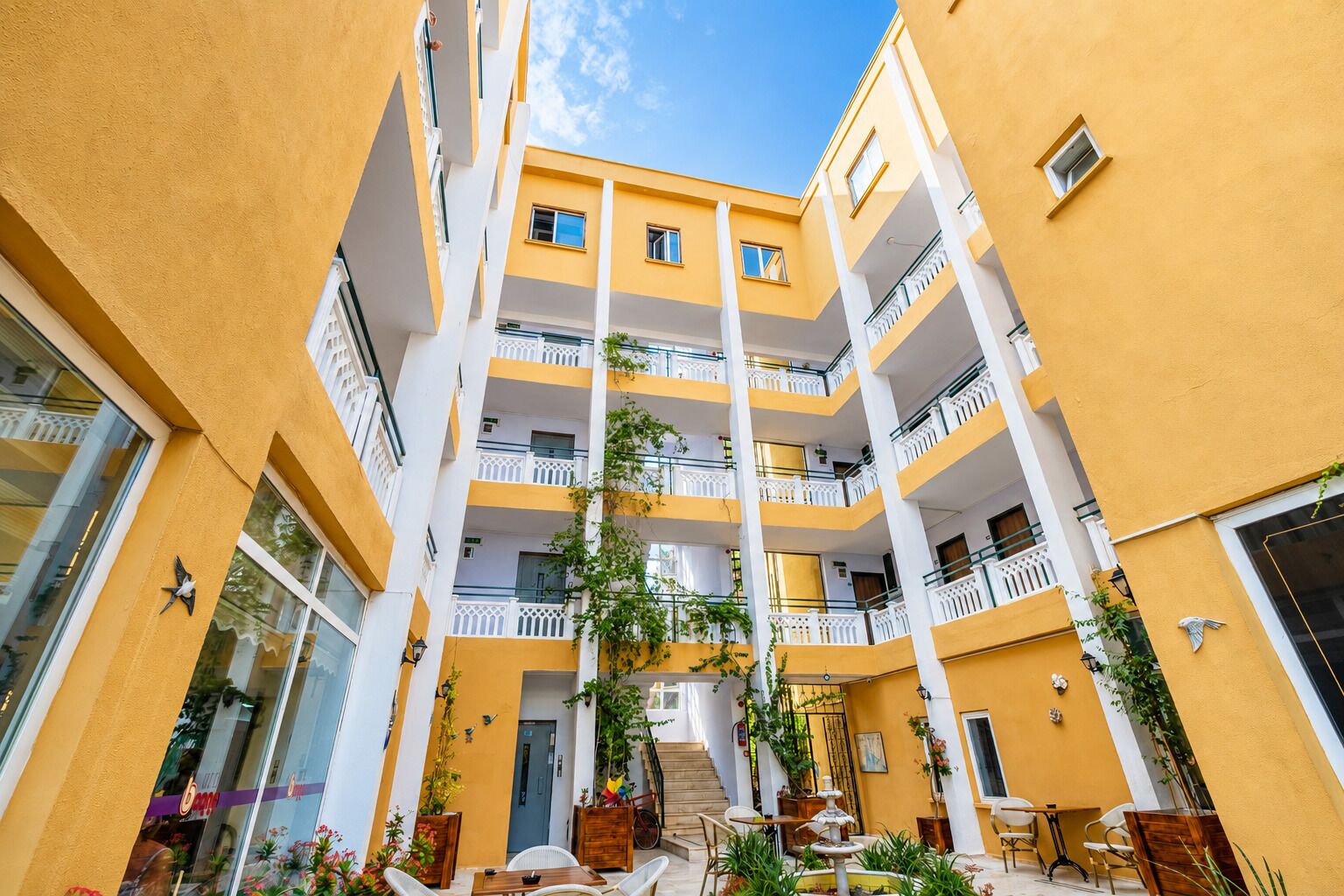 Un edificio de varios pisos con balcones, una escalera central y zonas de estar exteriores con plantas.