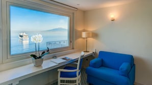 Une pièce avec une grande fenêtre, un bureau, une chaise, un canapé bleu et une lampe.