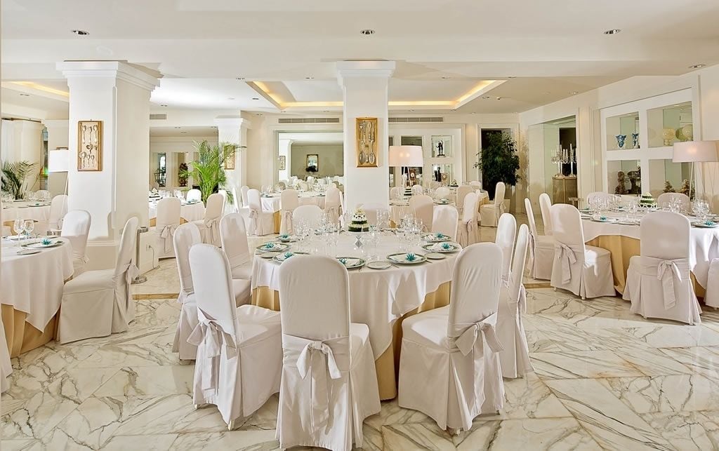 Une salle de banquet avec des tables rondes, des chaises blanches et un sol en marbre.