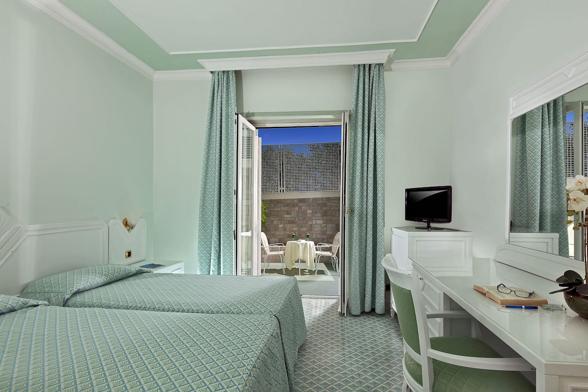 Ein Hotelzimmer mit zwei Betten, einem Schreibtisch mit Fernseher und einem Balkon mit Tisch und Stühlen.