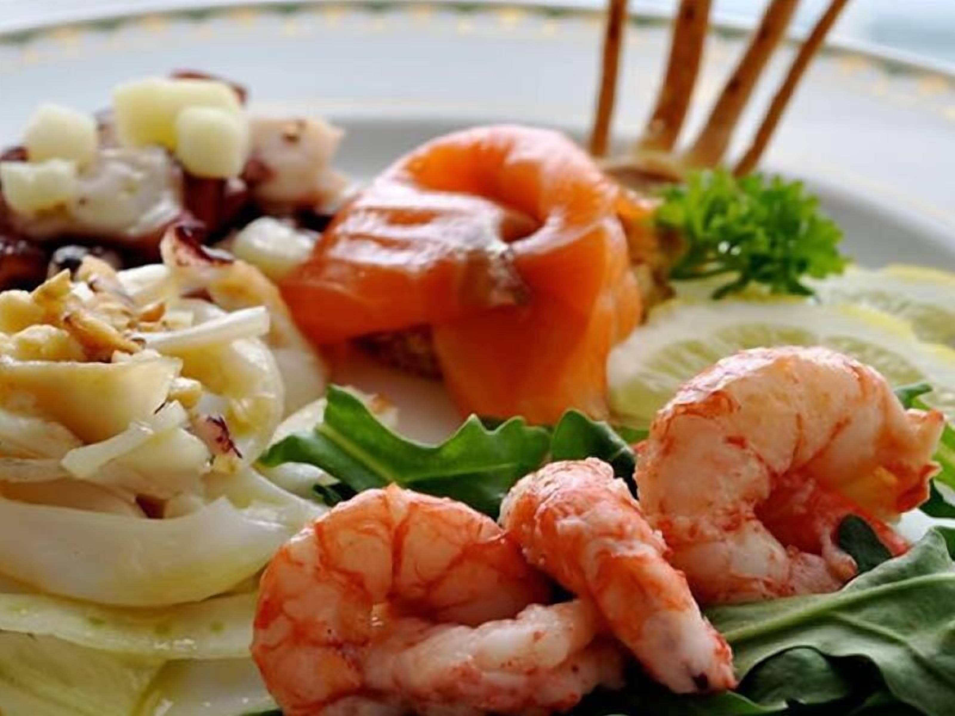 A plate of seafood including shrimp, salmon, and scallops, served with a side of greens.