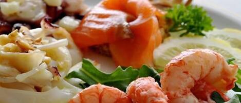 A plate of seafood including shrimp, salmon, and scallops, served with a side of greens.