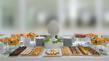 A buffet table with various pastries and desserts, including croissants, muffins, and a cake, arranged on plates and stands.