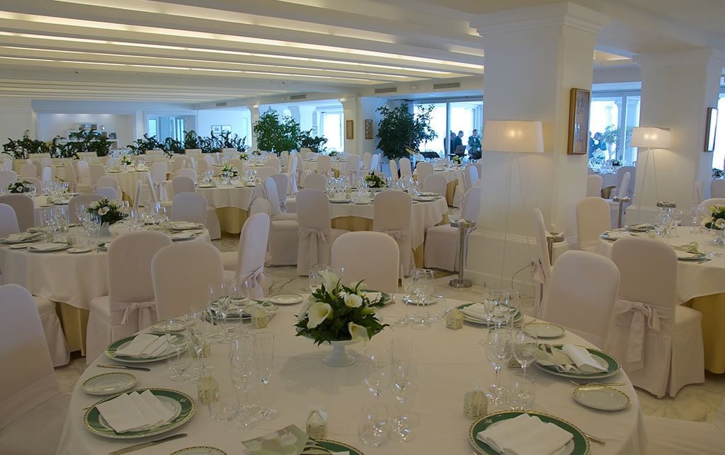 A banquet hall with round tables set with white tablecloths, green plates, and white napkins.