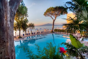 Un área de piscina con sillones y sombrillas, rodeada de árboles y vistas al mar.