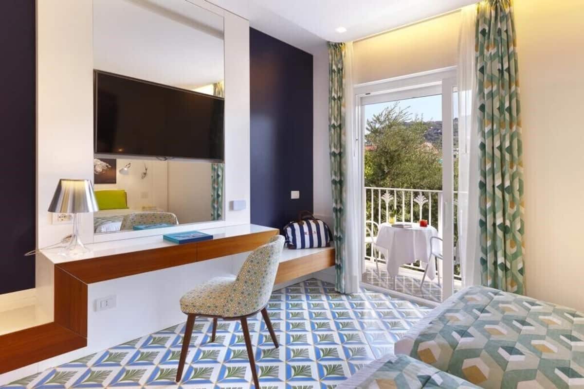 Ein Hotelzimmer mit Bett, Schreibtisch mit Stuhl, Fernseher und Balkon mit Tisch und Stühlen.