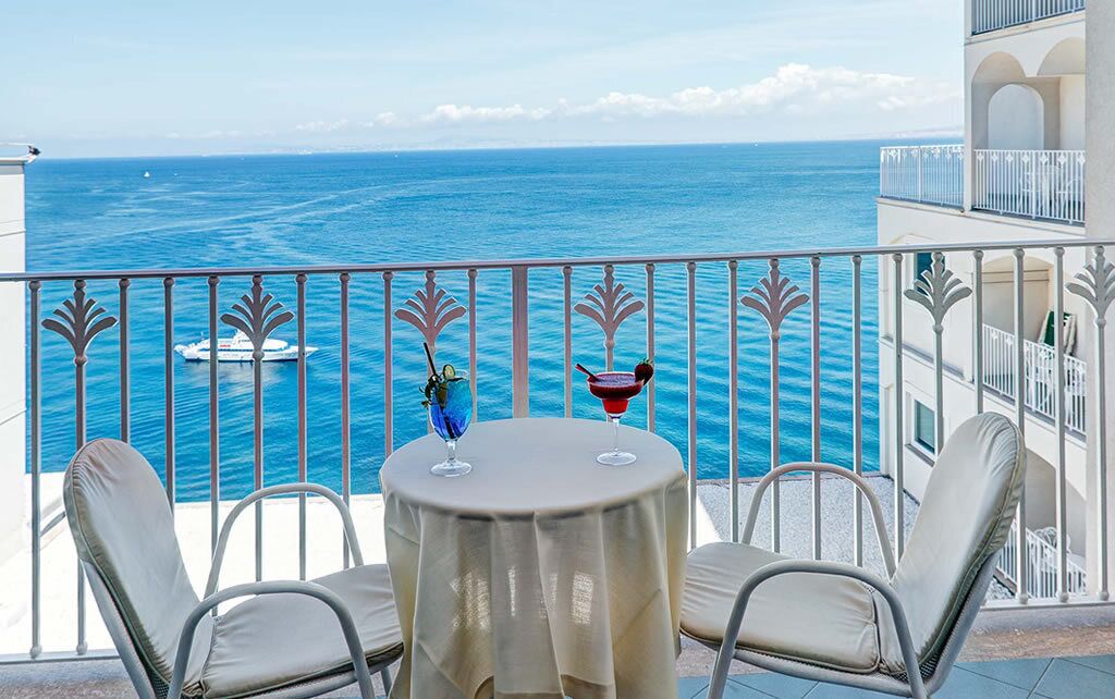 Ein Balkon mit Tisch und Stühlen, mit Blick auf das Meer und ein Boot in der Ferne.