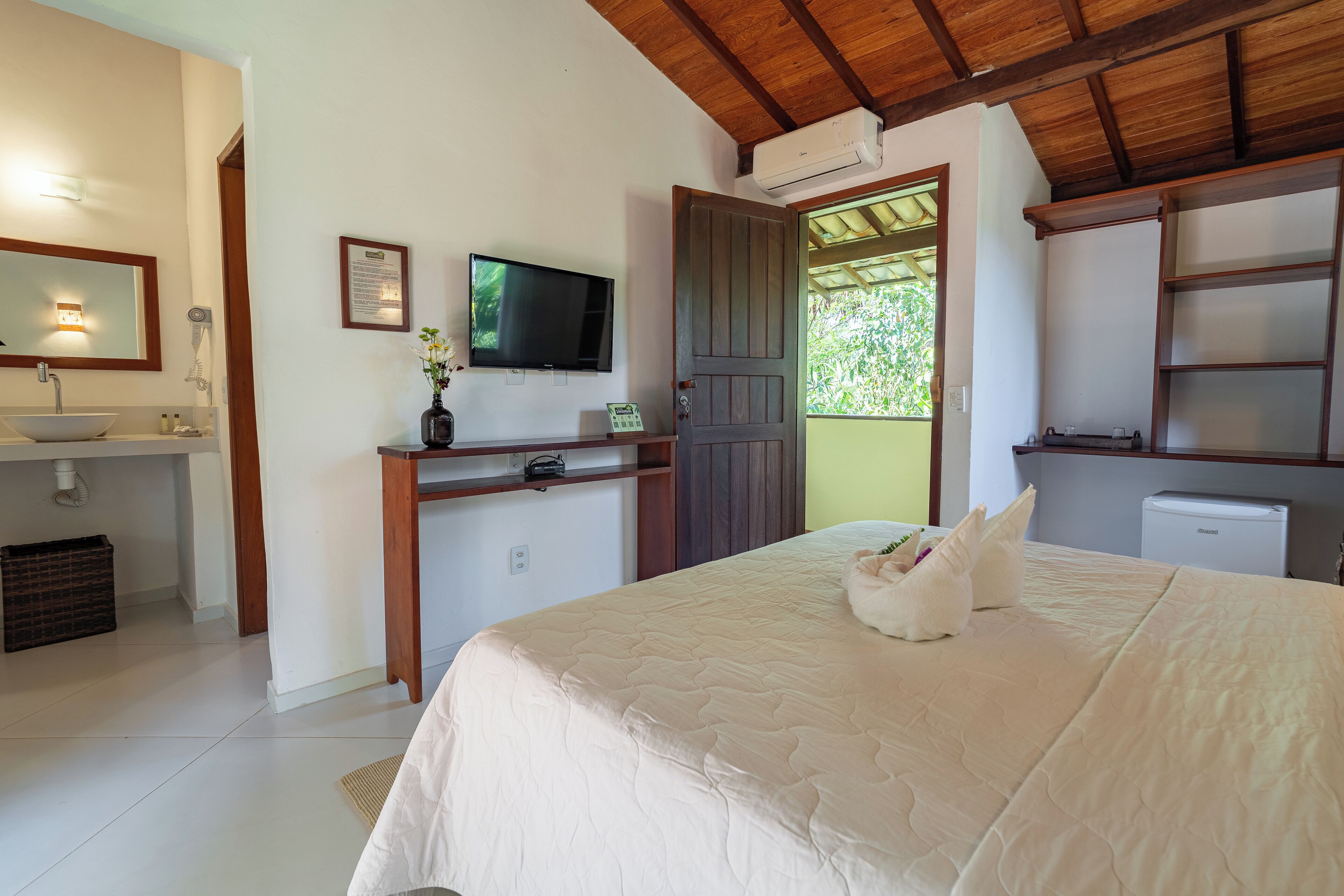 Une chambre à coucher comprenant un lit, une table de chevet, un téléviseur, un bureau avec une chaise, une fenêtre et une salle de bain avec un lavabo et des toilettes.