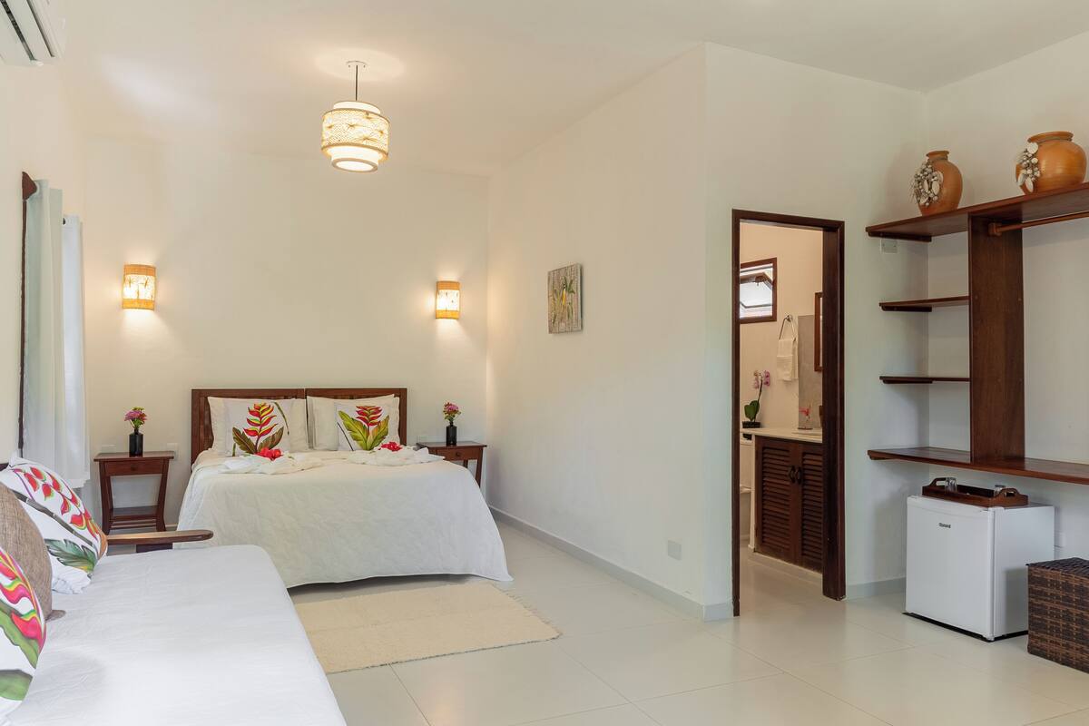 A bedroom with a bed, bedside tables, a nightstand, a dresser, and a small refrigerator.