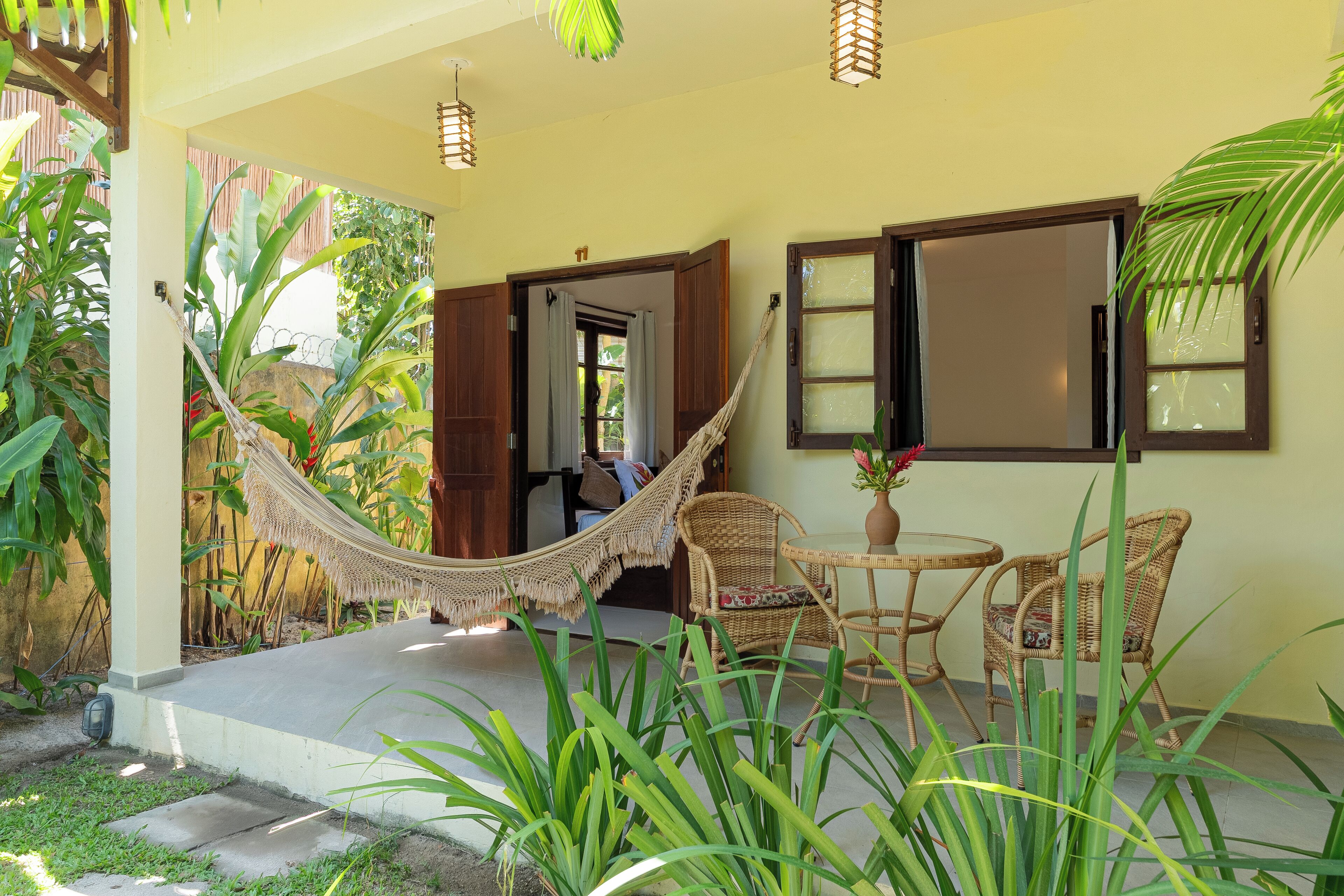 A covered outdoor seating area with wicker furniture, a hammock, and potted plants.