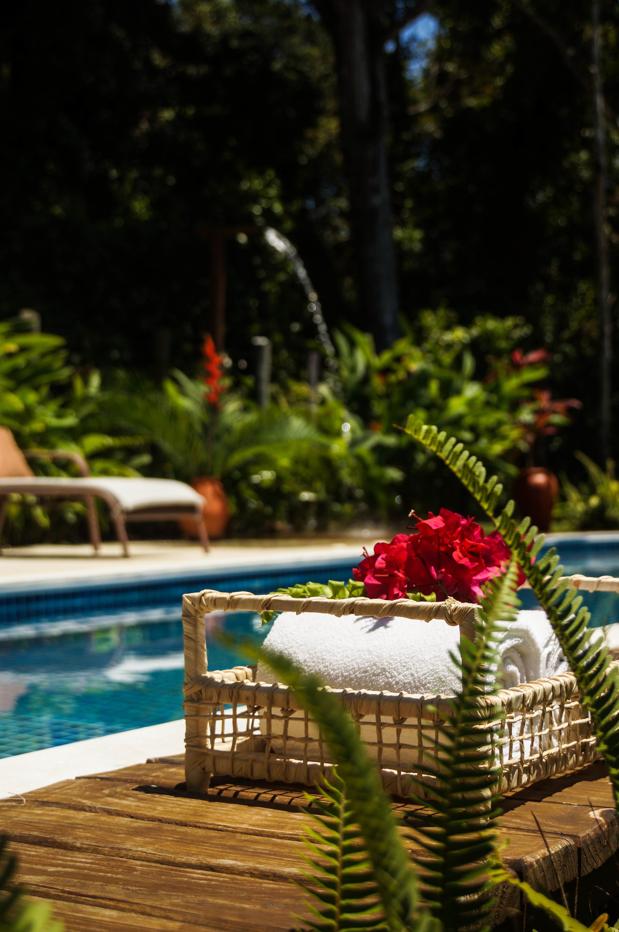 Uma área junto à piscina com uma cadeira de vime e um objeto decorativo com flores vermelhas.