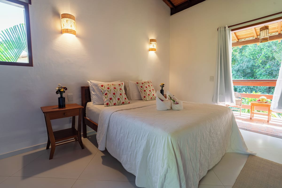 A bedroom with a large bed, two wall-mounted lights, a nightstand, and a view of the outdoors.