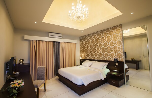 A modern hotel room with a large bed, a desk with a computer, a chair, and a chandelier.