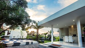 A modern outdoor area with a seating area, steps leading to a covered section, and a stone wall with a computer. - Noah Villa and Chapel (Ungasan)