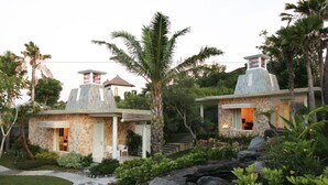 A two-story house with a stone facade, a small porch, and a garden with palm trees and shrubs. - Noah Villa and Chapel (Ungasan)