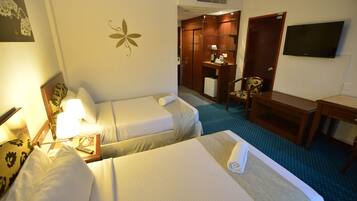 Habitación de hotel con dos camas, un escritorio, una silla, televisión y baño con espejo y armario.