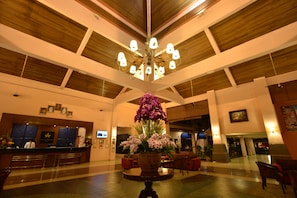 A spacious lobby with a wooden ceiling, a reception desk, and a large floral arrangement.