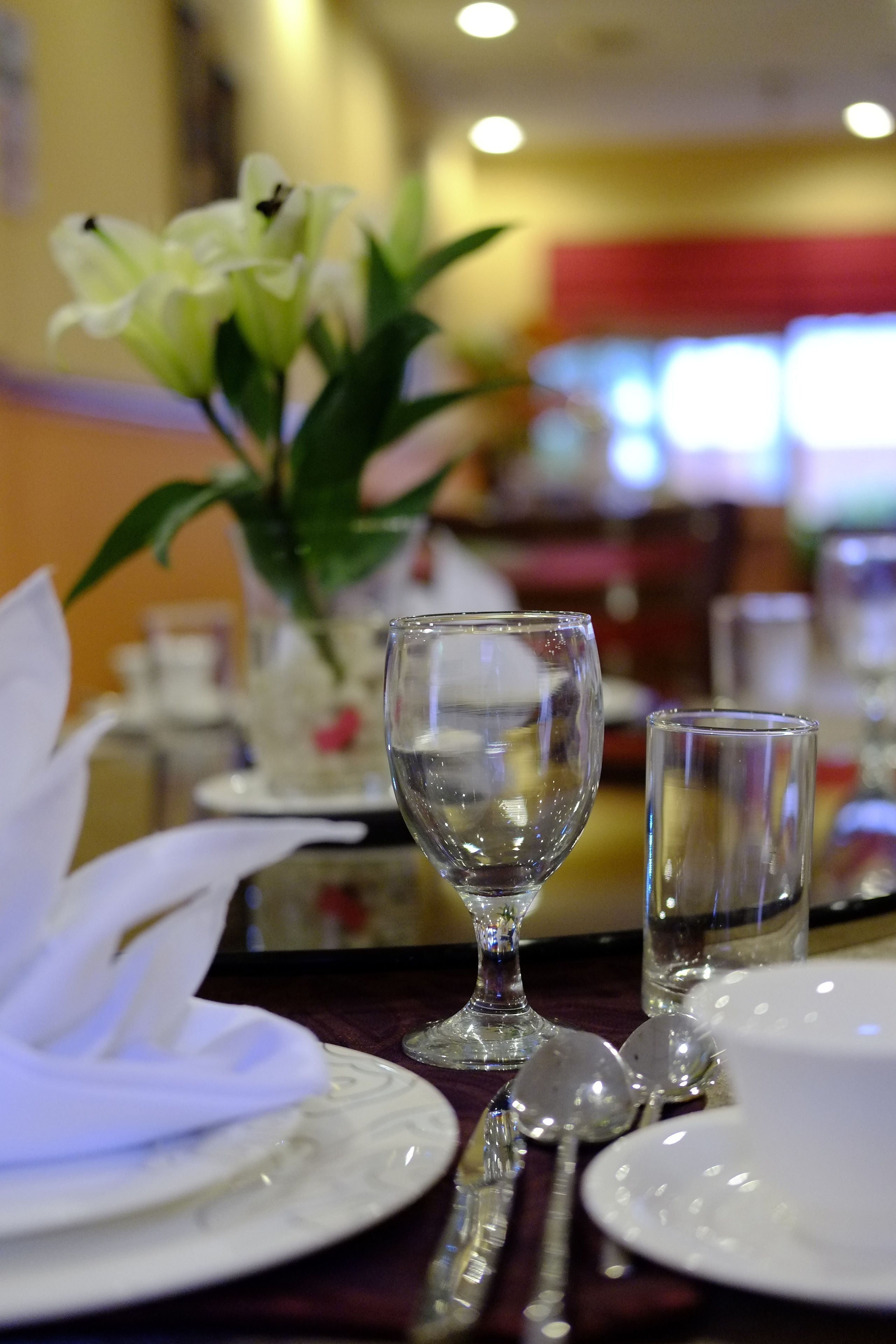 A dining table set with a white napkin, a clear wine glass, a white plate, and a spoon.