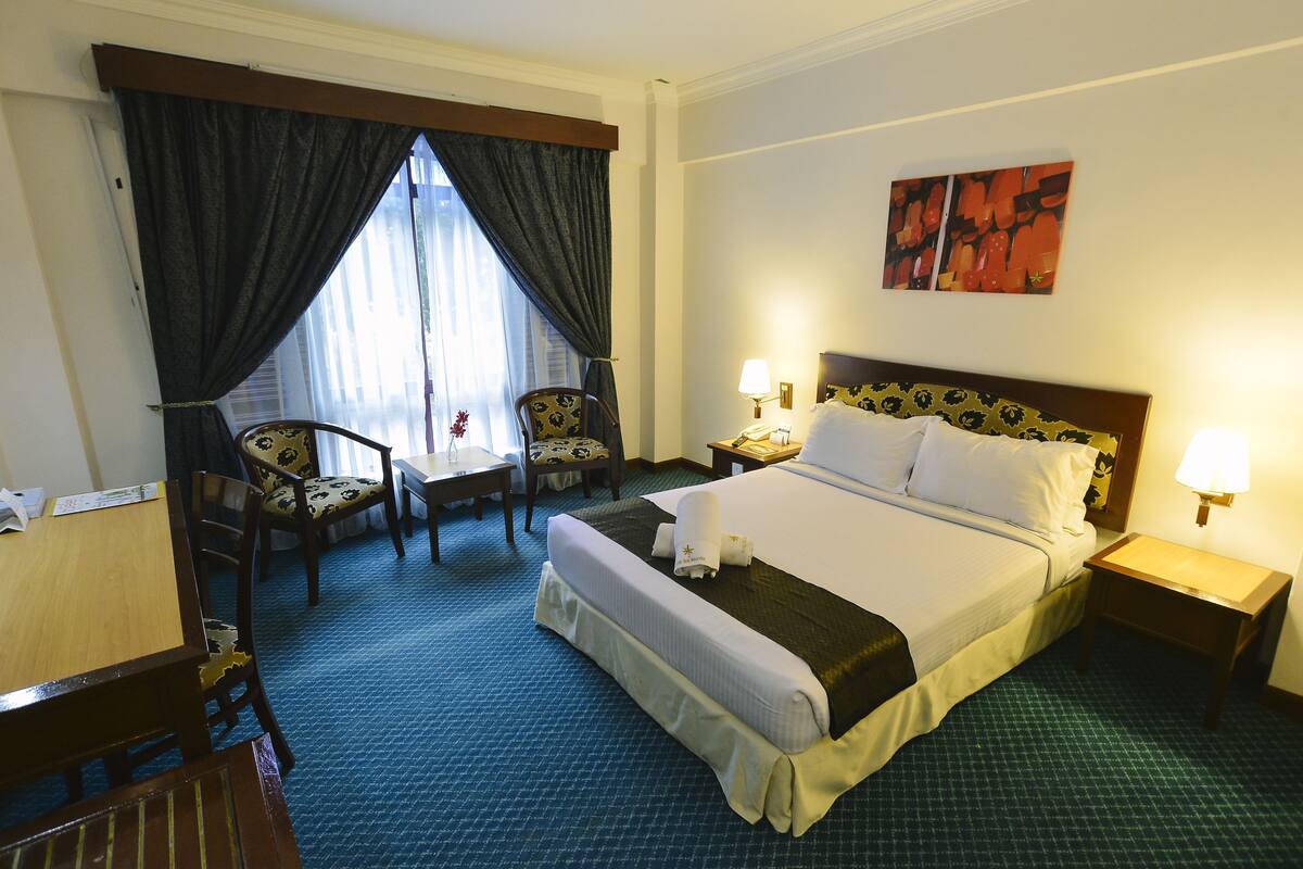 A hotel room with a bed, two bedside tables, a chair, a desk, and a window with curtains.