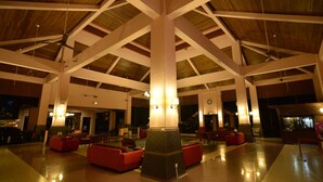 Een ruime lobby met hoge plafonds, rode zitplaatsen en een centrale kolom.