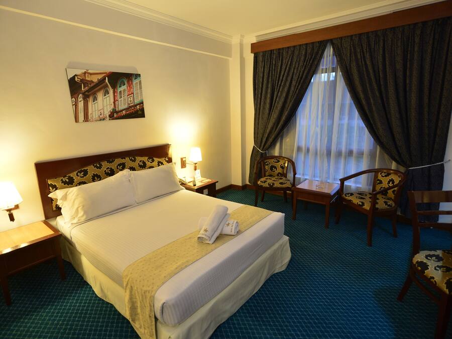 Une chambre d’hôtel avec un grand lit, deux tables de chevet avec des lampes, une chaise et une fenêtre avec des rideaux.