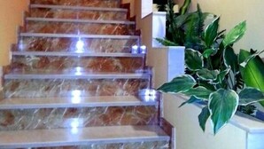 A marble staircase with a handrail, leading to a landing with a white wall and a plant. - Hotel Castilla (Antequera)