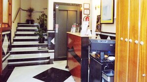 A hotel lobby with a staircase, reception desk, and a door leading to an elevator. - Hotel Castilla (Antequera)