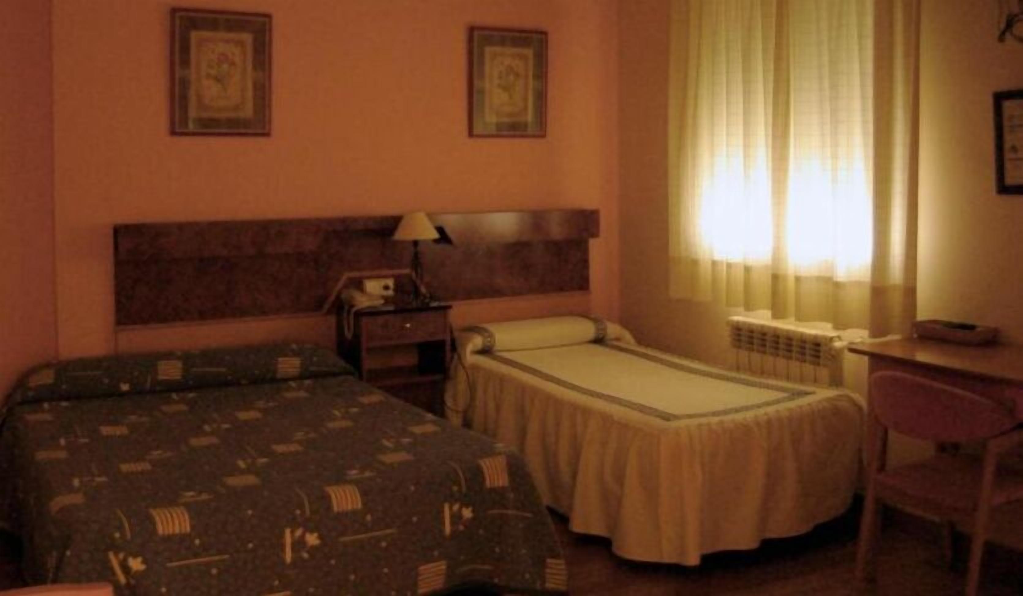 Habitación de hotel con dos camas, un escritorio, una silla y una ventana con cortinas.