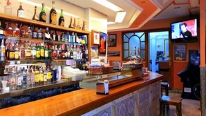 A bar area with shelves of liquor bottles, a counter with a cash register, and a television screen. - Hotel Castilla (Antequera)