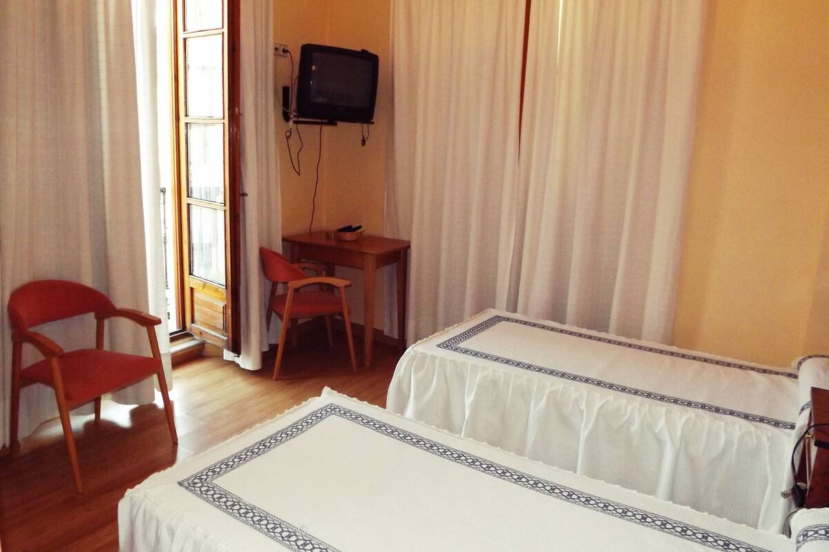 Una habitación con dos camas, un escritorio, una silla y un televisor montado en la pared.