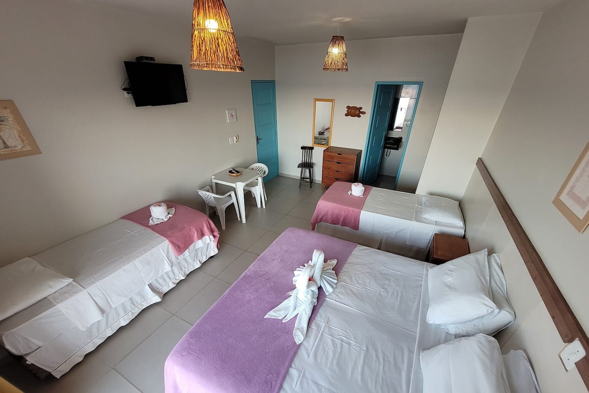 Habitación de hotel con cuatro camas, un escritorio y una silla. Hay un televisor montado en la pared y una puerta que da a otra habitación.