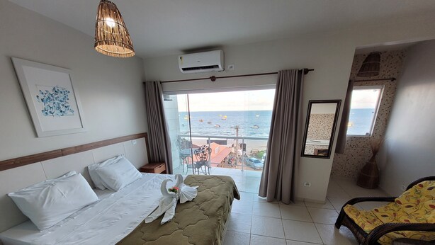 Een hotelkamer met een bed, een stoel, een balkon met uitzicht op zee en een wandairconditioner.