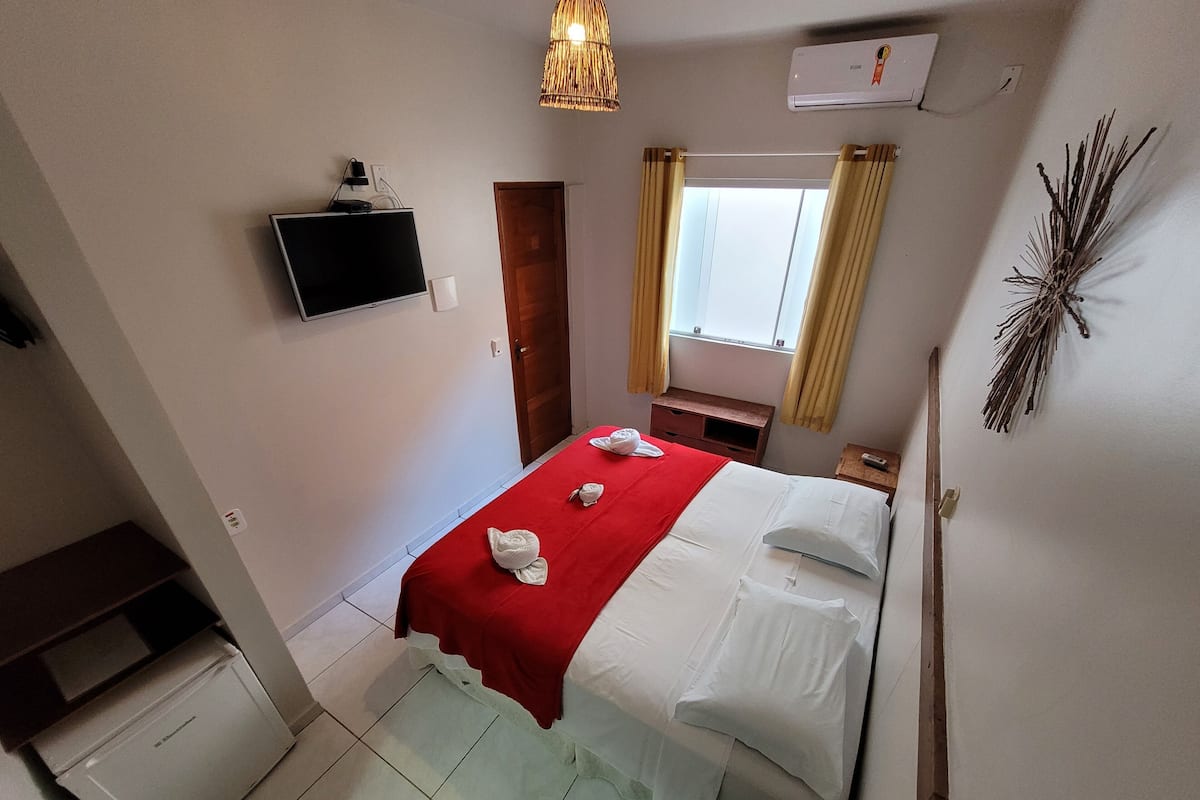 Habitación de hotel con cama, televisor montado en la pared, escritorio, ventana con cortinas y equipo de aire acondicionado.