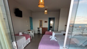 Een hotelkamer met balkon, een bed met paars beddegoed, een bureau met stoel en een televisie aan de muur.