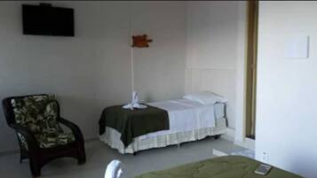 Una habitación pequeña y sencilla con cama, una silla y un ventilador de pie.