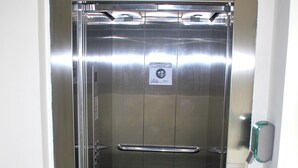 Een metalen lift met een groen tapijt, een handgreep en een bordje op de deur.