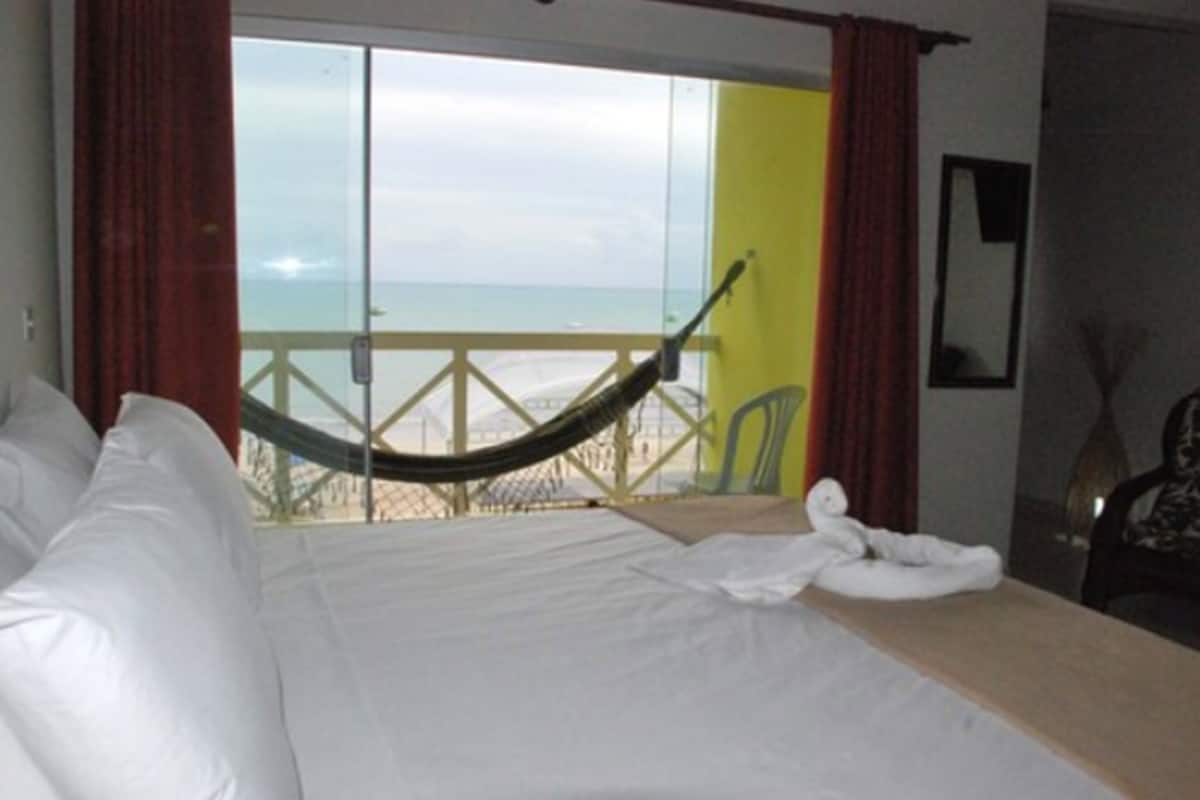 Una habitación de hotel con cama, una hamaca y vista a la playa.