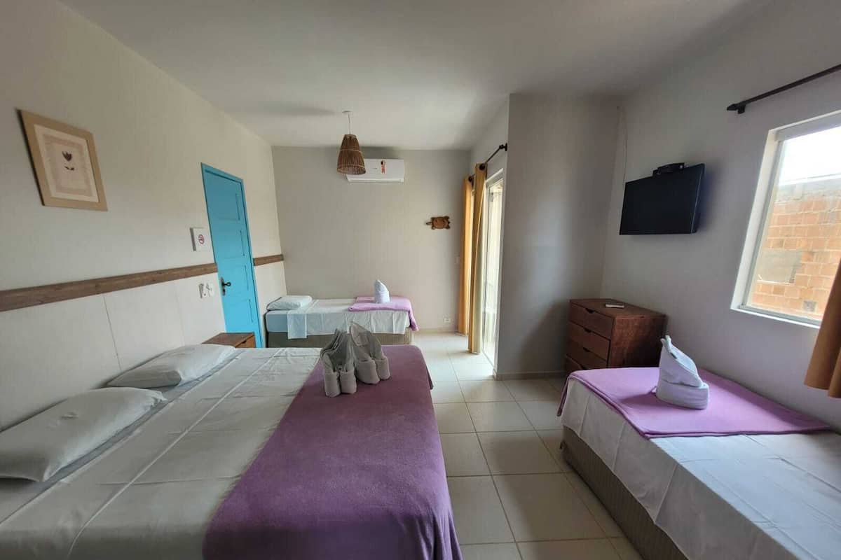 Habitación de hotel con dos camas individuales, un aparador de madera, un televisor montado en la pared y una ventana con cortinas.