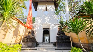 Um edifício com fachada branca, uma bandeira vermelha e duas estátuas de Buda nos degraus.